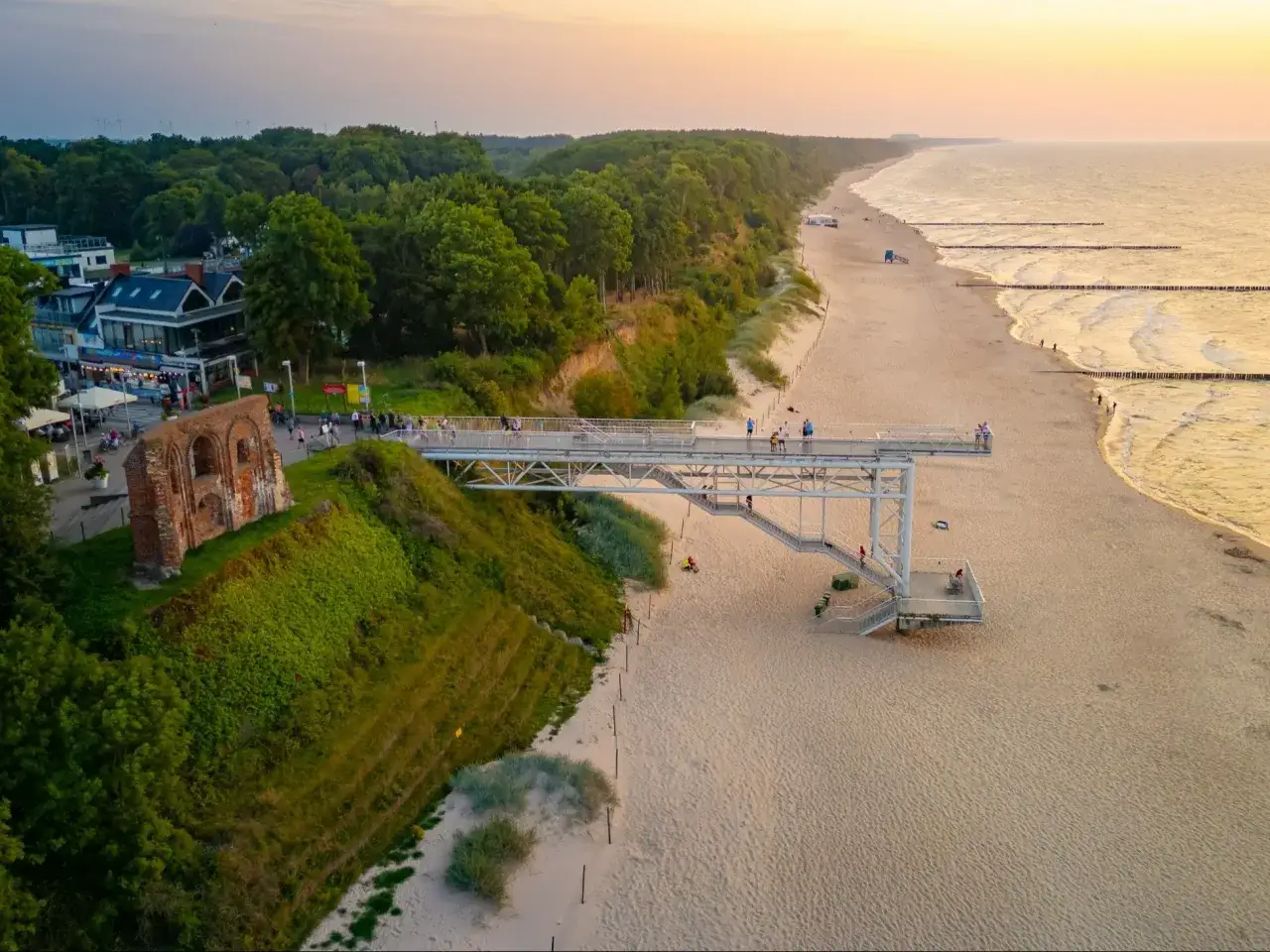 Zach&oacute;d słońca nad Bałtykiem. Widok na plażę, klif z ruinami i kładkę widokową. Czy można spać na plaży? Tu na pewno nie, ale widok zachwyca.