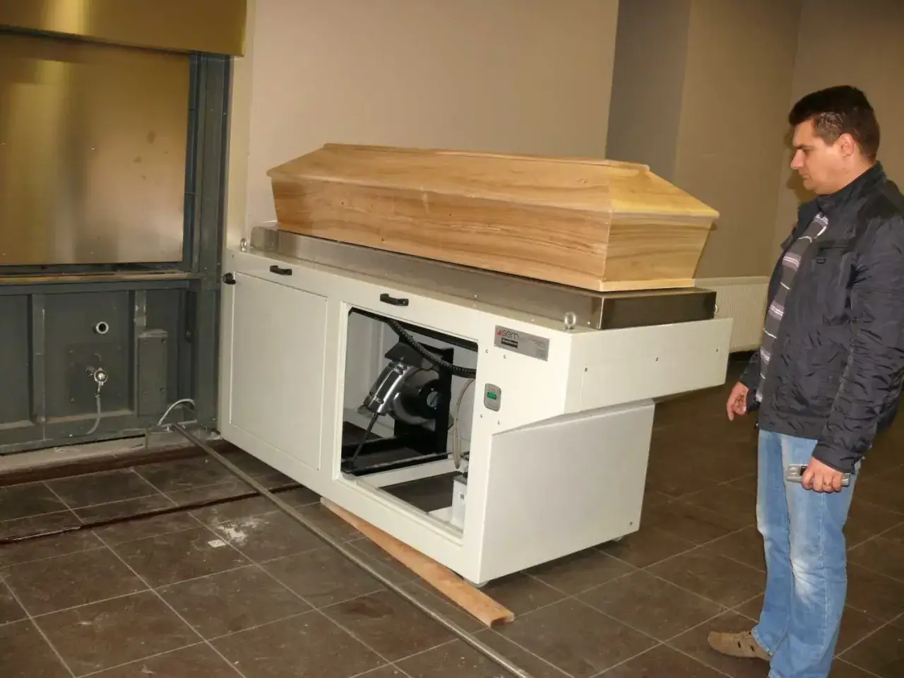 Mężczyzna obserwuje trumnę na kremacyjnej maszynie. Czy kremacja boli zmarłego? Nie, proces jest bezbolesny.