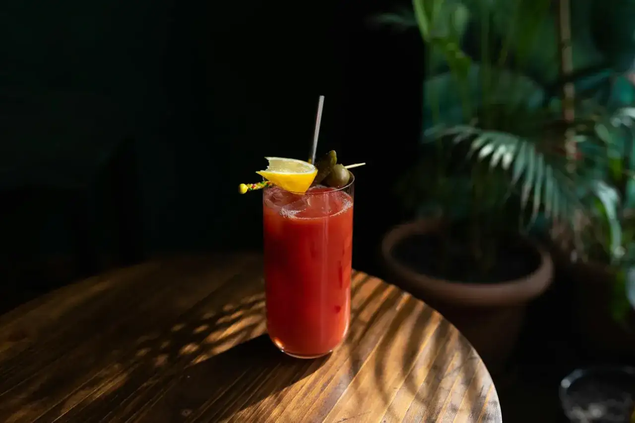 Idealny Krwawa Mary przepis na orzeźwiający drink. W szklance czerwony koktajl z lodem, cytryną, oliwką i ogórkiem.