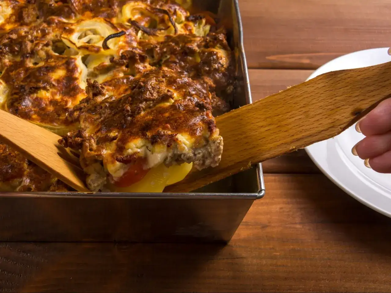 Zapiekanka ziemniaczana z mięsem mielonym, idealna na obiad. Ktoś nakłada porcję na talerz.