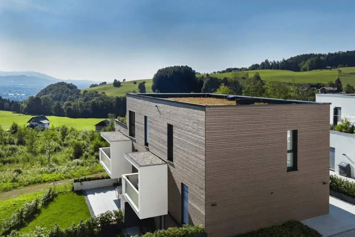 Nowoczesny, mały dom z płaskim dachem porośniętym zielenią, otoczony malowniczymi wzgórzami i polami.