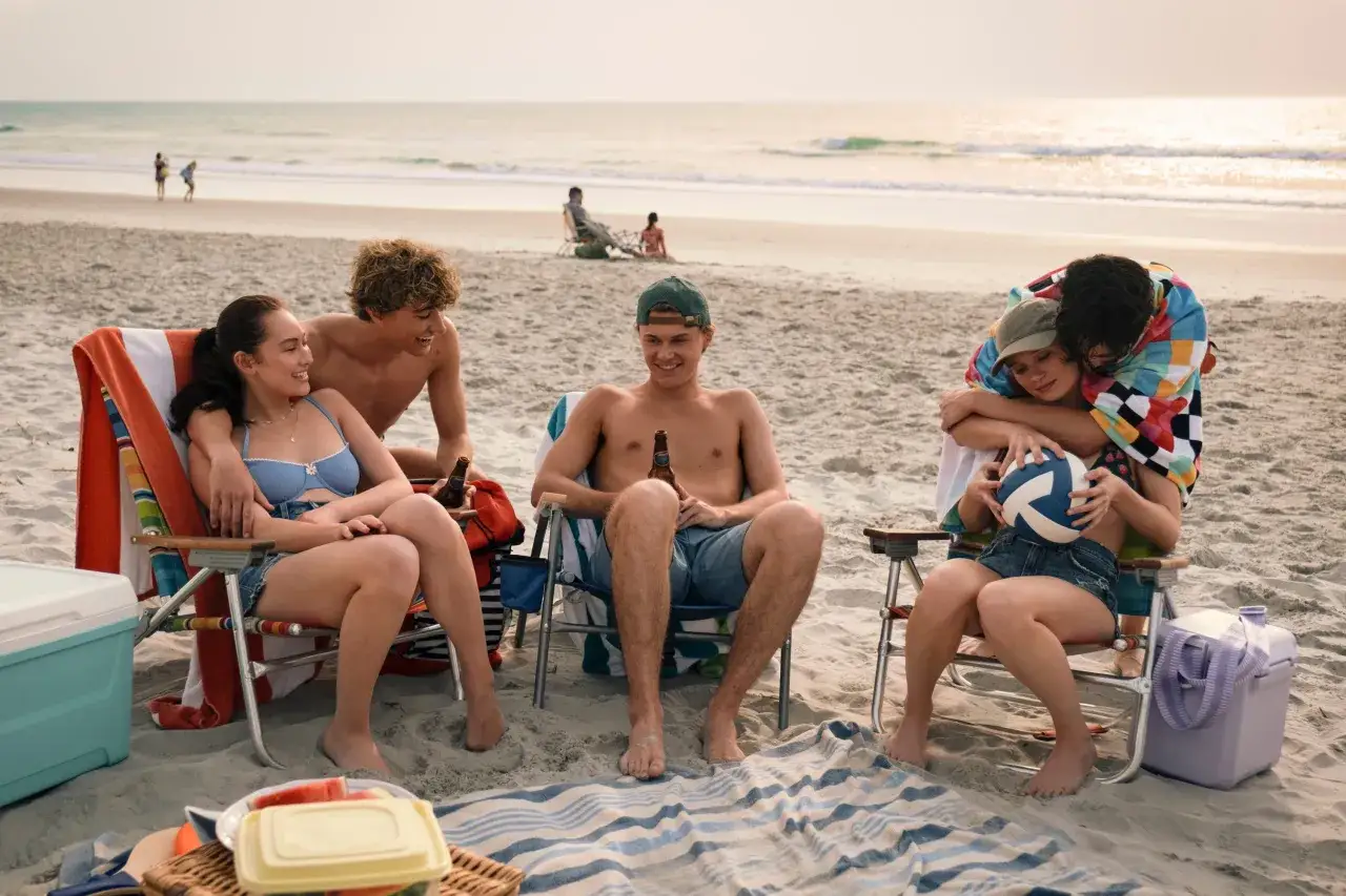 Młodzi ludzie cieszą się latem na plaży, pijąc napoje i przytulając się. To idealny moment, by poczuć się jak w serialu 