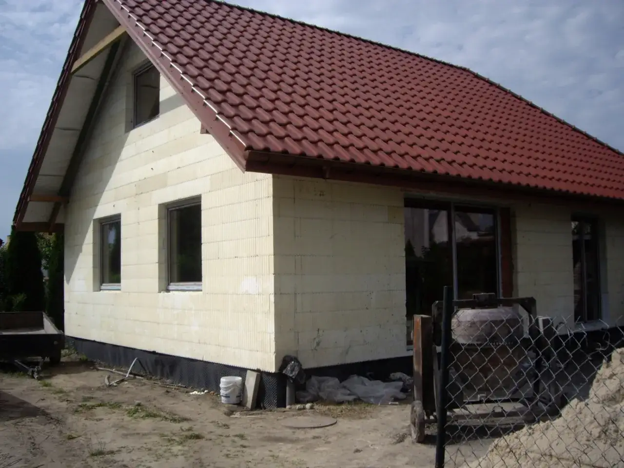 Budowa domu ze styropianu z czerwonym dachem. Widać okna, fundamenty i plac budowy.