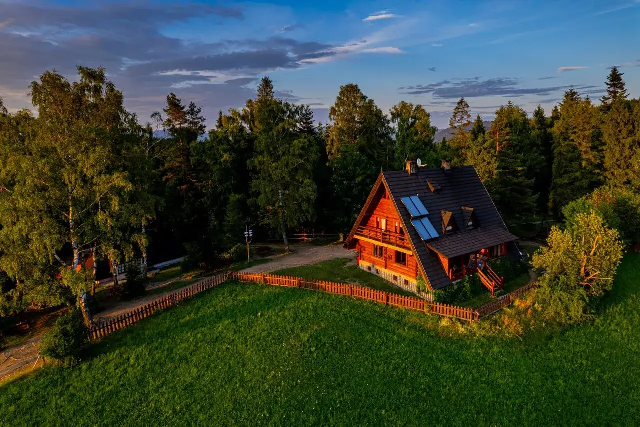 Drewniana bac&oacute;wka na Maciejowej, otoczona zieloną łąką i lasem, w blasku zachodzącego słońca.