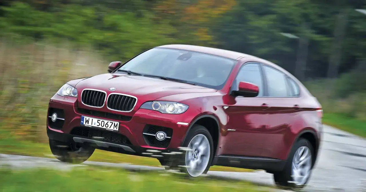 Czerwone BMW X6 pędzi po krętej drodze, otoczone rozmytą zielenią. Oto moto w akcji!