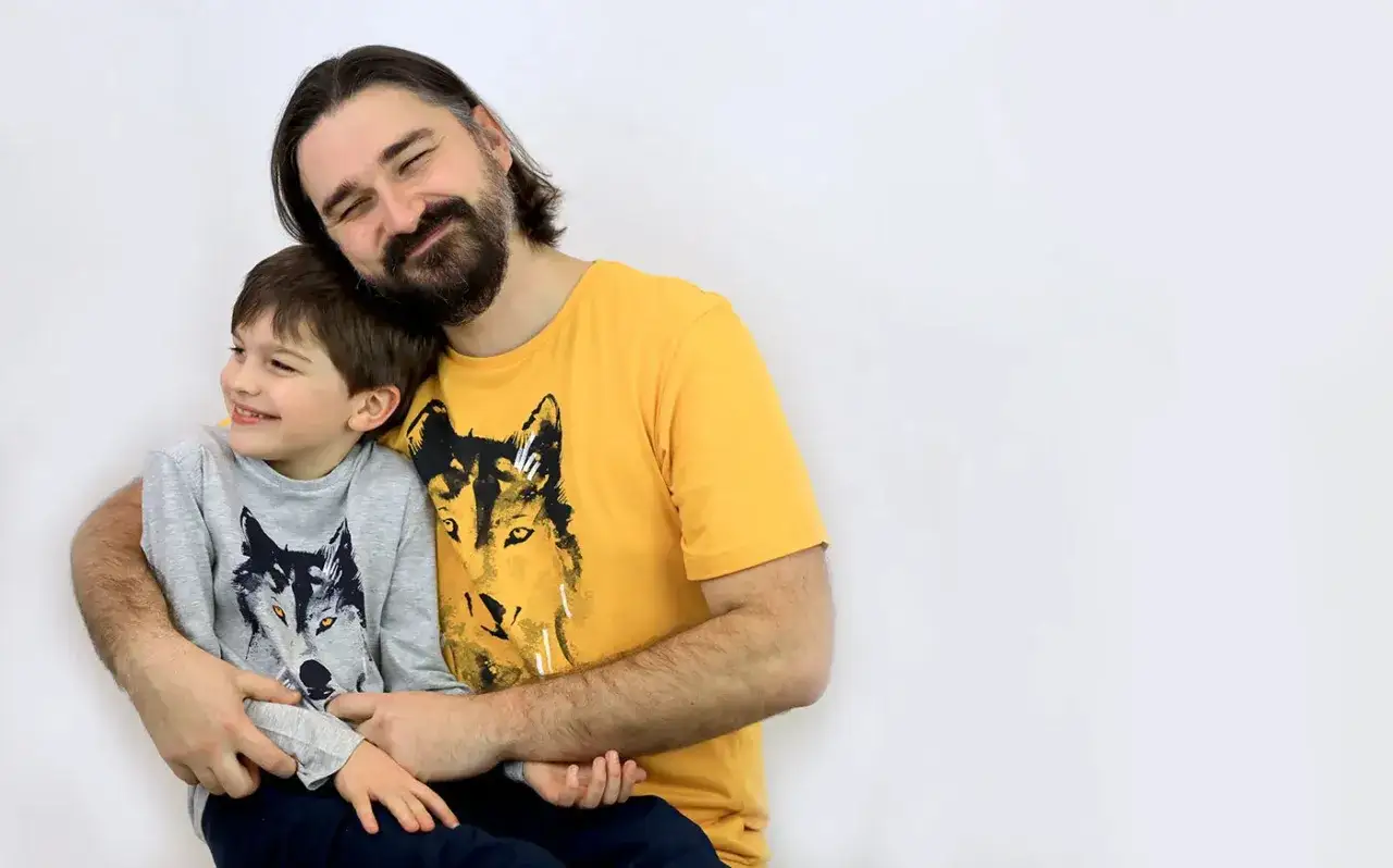 Tata obejmuje swojego synka, obaj uśmiechnięci. Na ich koszulkach widnieją wilki, jakby tworzyli zgraną watahę.