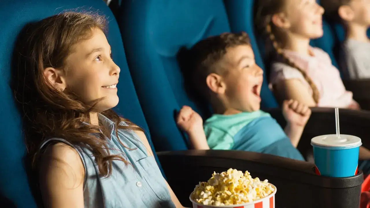 Dzieci śmieją się i jedzą popcorn podczas oglądania komedii dla dzieci w kinie.