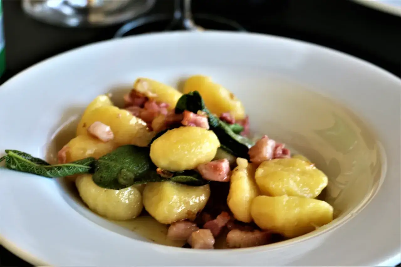 Pyszne gnocchi z boczkiem i szałwią, podane na białym talerzu.