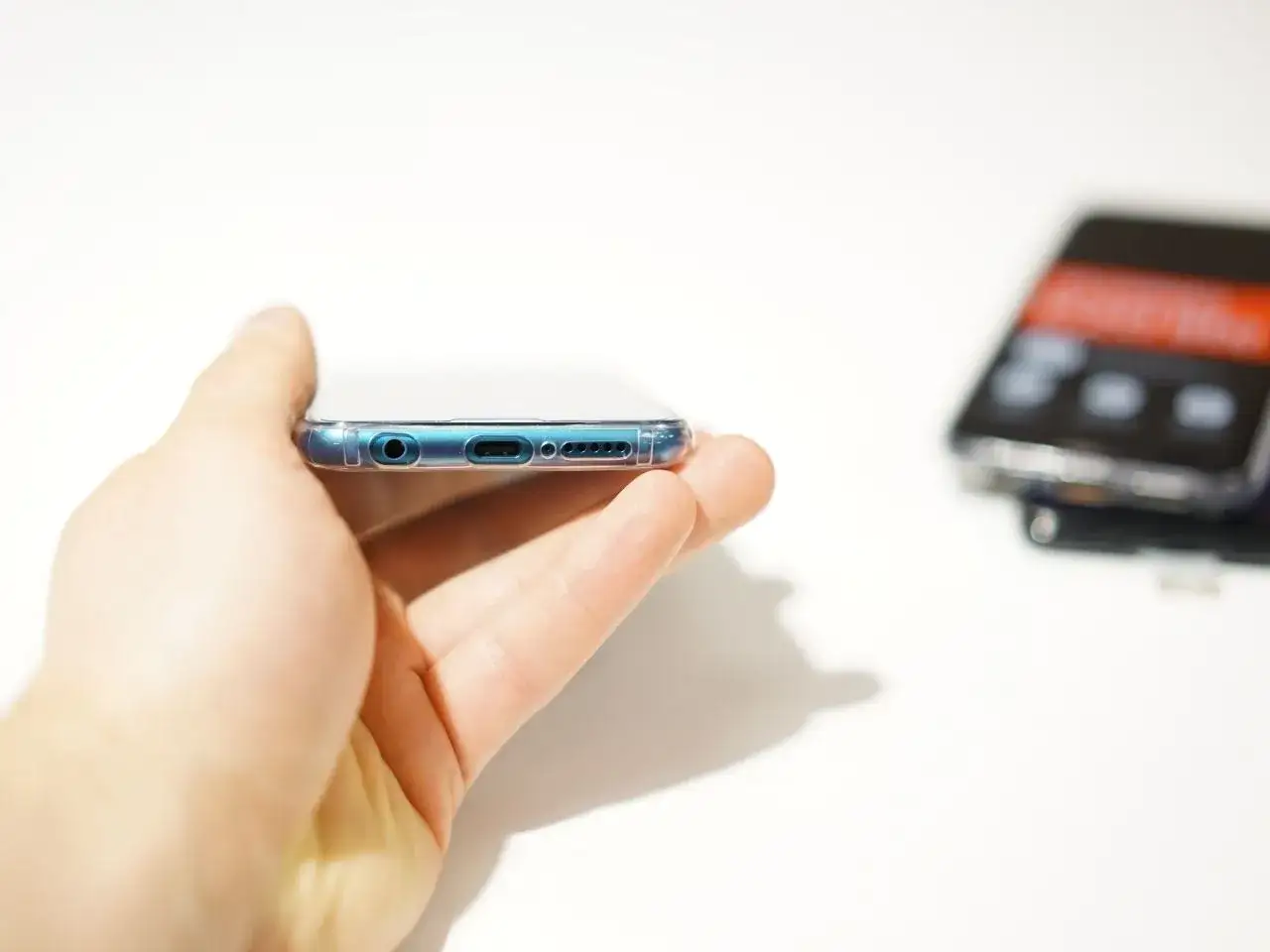 Dłoń trzyma smartfon z widocznym gniazdem słuchawkowym i portem ładowania. W tle drugi telefon. Czy to HMS Core?