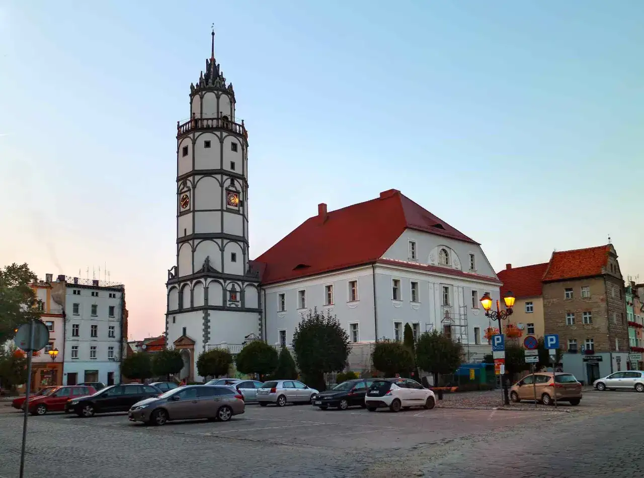 Wieża ratuszowa i zabytkowe kamienice to gł&oacute;wne paczk&oacute;w atrakcje. Na rynku zaparkowane są samochody.