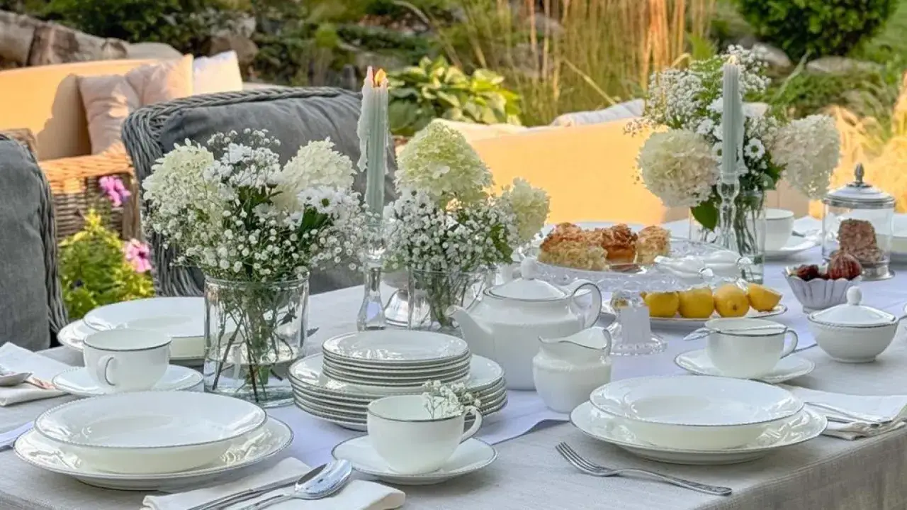 Elegancka patera ceramiczna z ciastkami i owocami, otoczona białymi kwiatami i zastawą stołową, tworzy scenerię letniego podwieczorku.