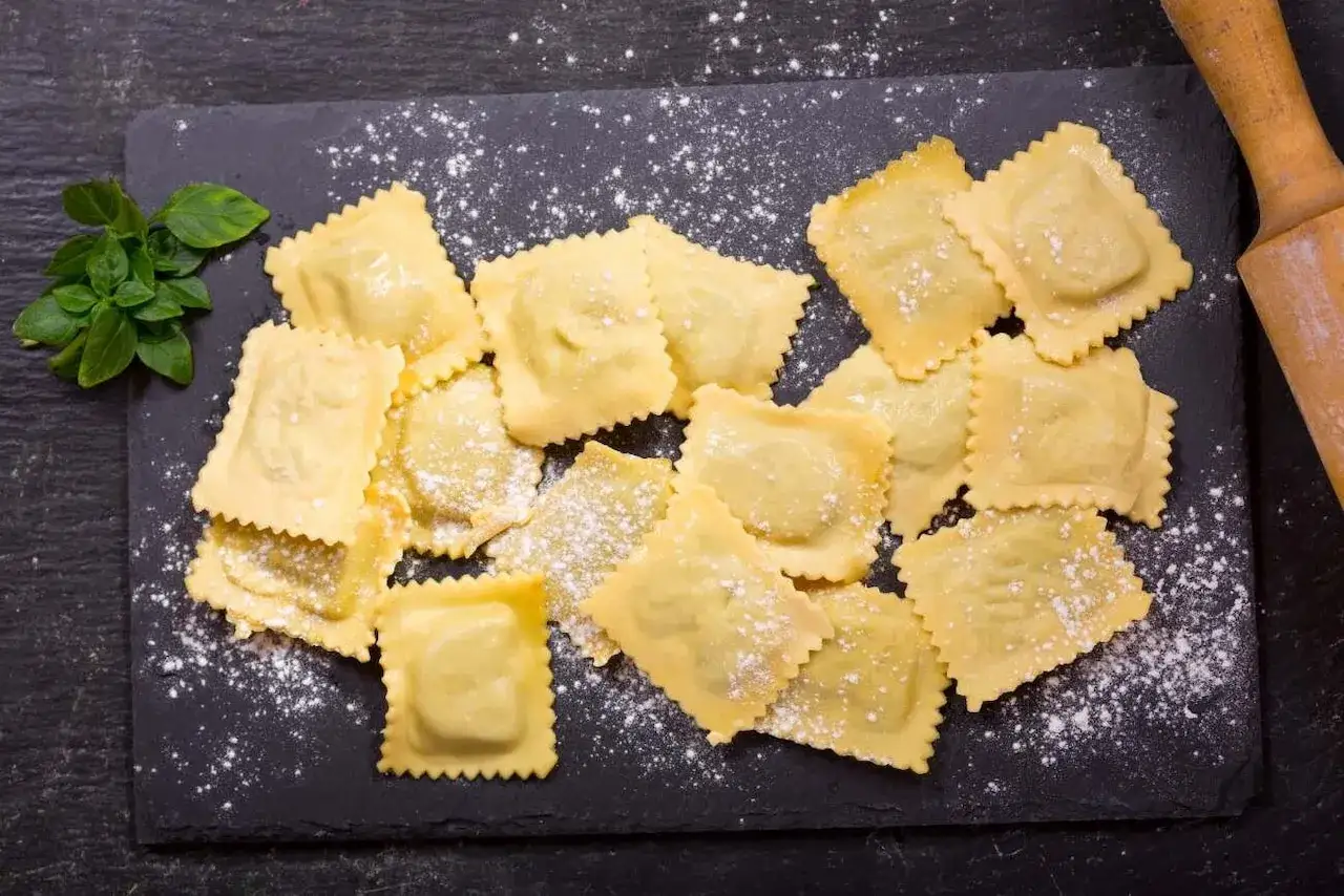 Świeże ravioli, gotowe do gotowania. Idealny przepis na domowe ravioli, z bazylią i wałkiem w tle.