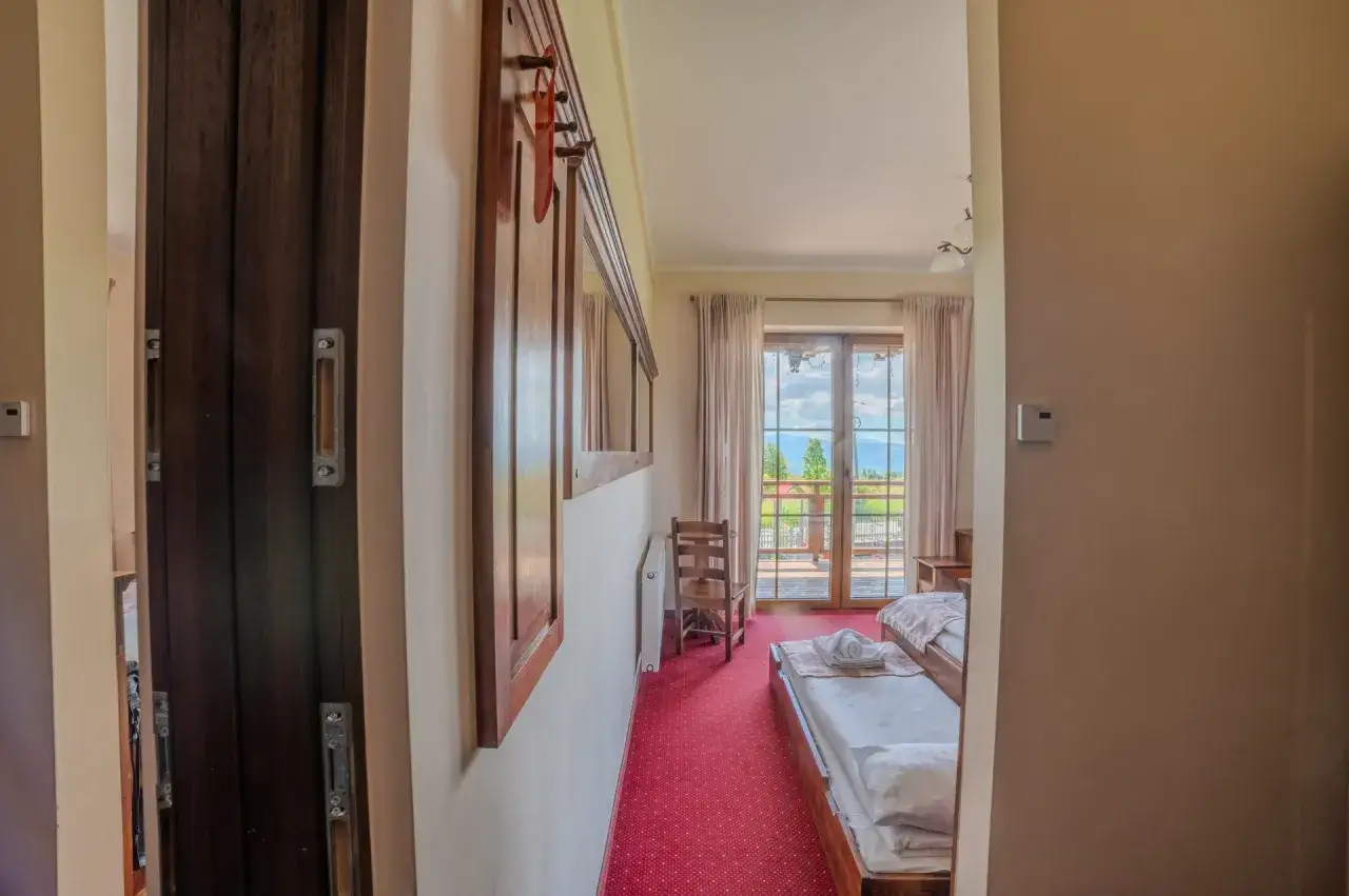 Pokój z widokiem na góry, gdzie można poczuć klimat szarotki bukowina tatrzańska. Dwa łóżka, drewniane meble i czerwony dywan.