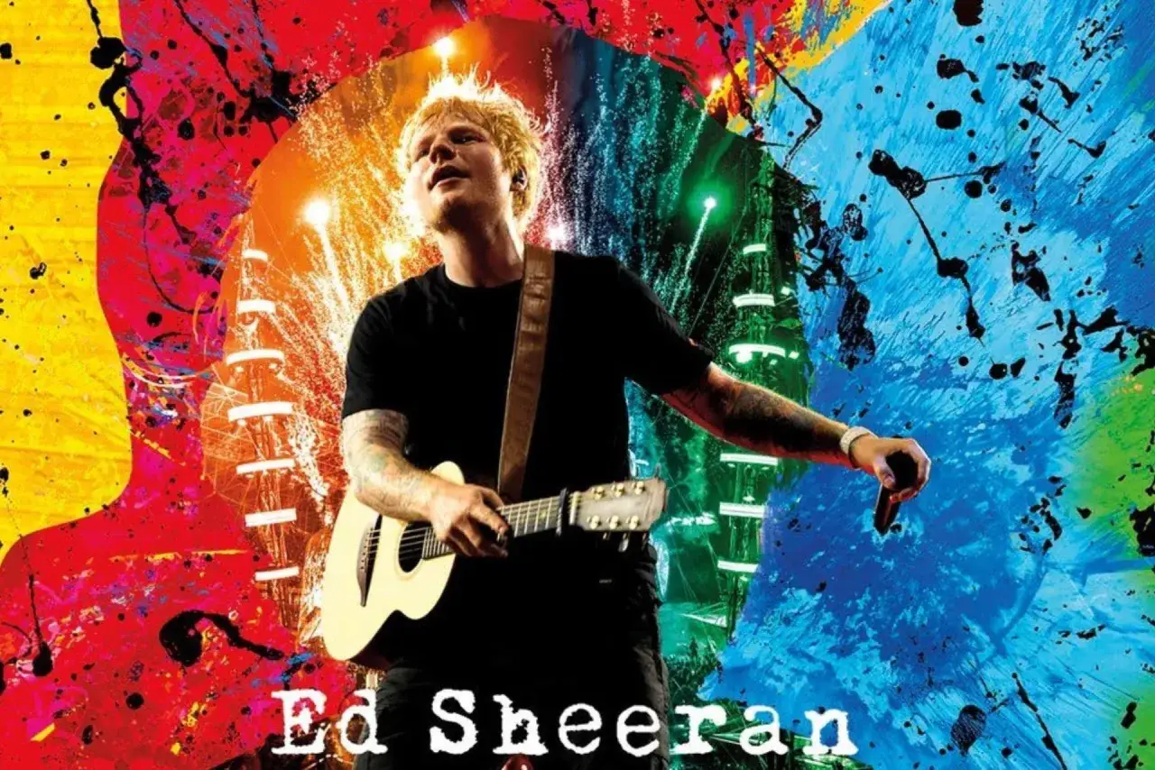 Ed Sheeran z gitarą i mikrofonem, w otoczeniu kolorowych eksplozji farby. Marzenie o koncercie kiedy Ed Sheeran zagra koncert w Polsce.
