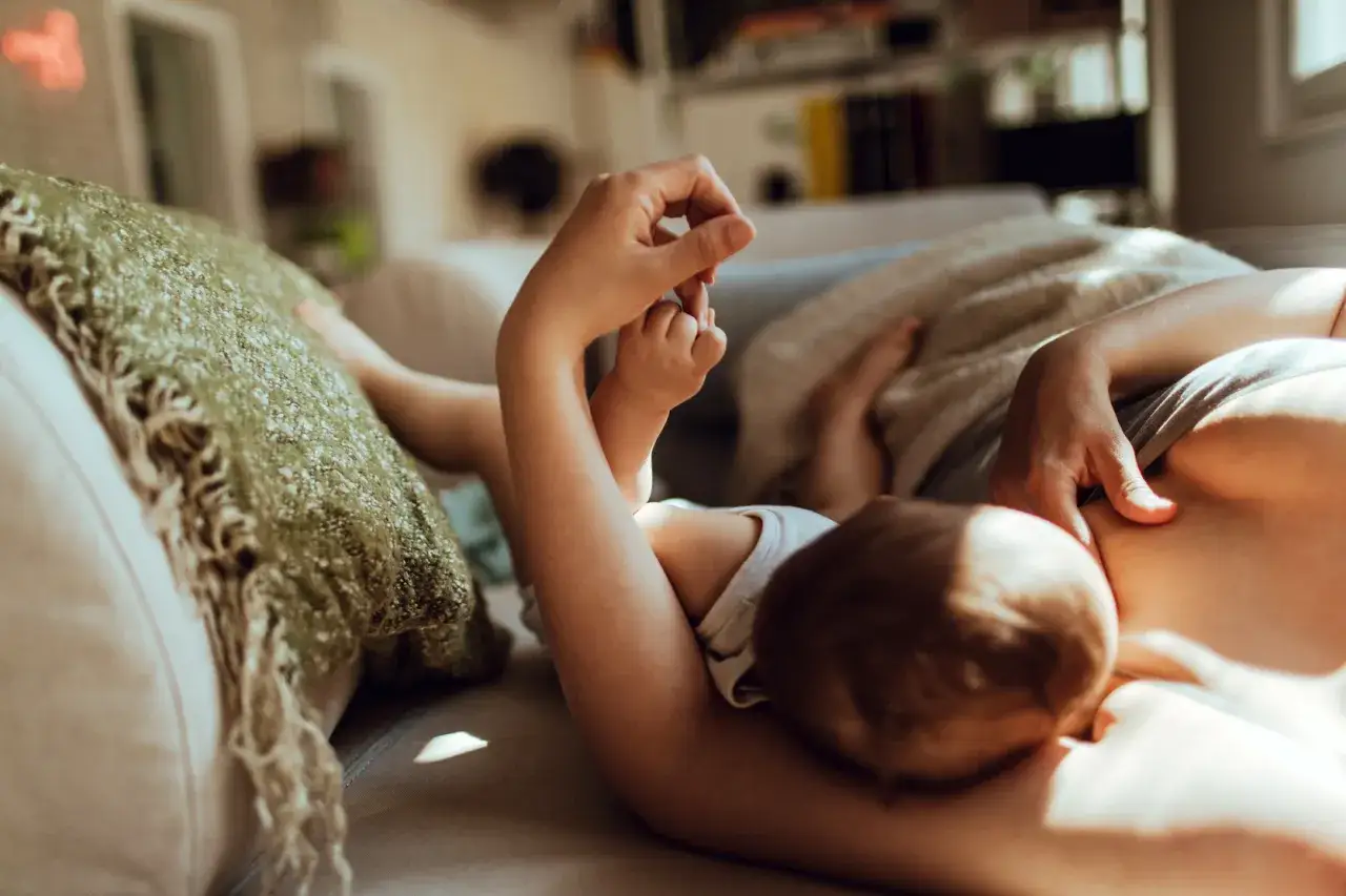 Mama karmi na leżąco, a maluch wyciąga rączki. Po karmieniu przyjdzie czas na odbijanie.