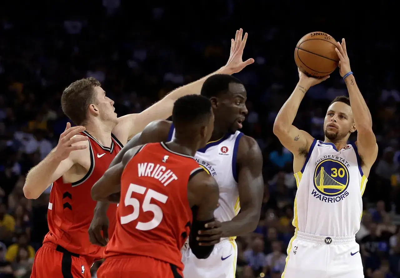 Stephen Curry, silny skrzydłowy, szykuje się do rzutu. Obrońcy pr&oacute;bują go zatrzymać.
