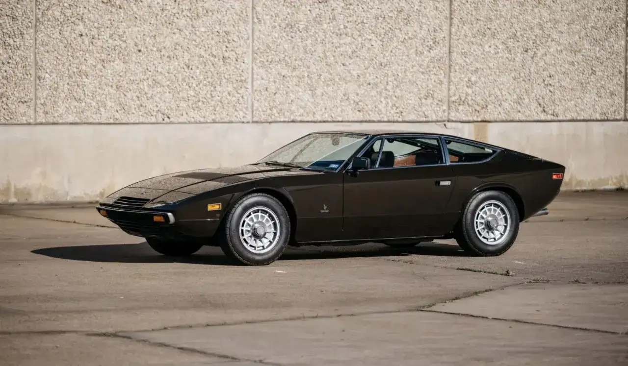 Klasyczny, brązowy Maserati Shamal z lat 90. na tle kamiennej ściany.