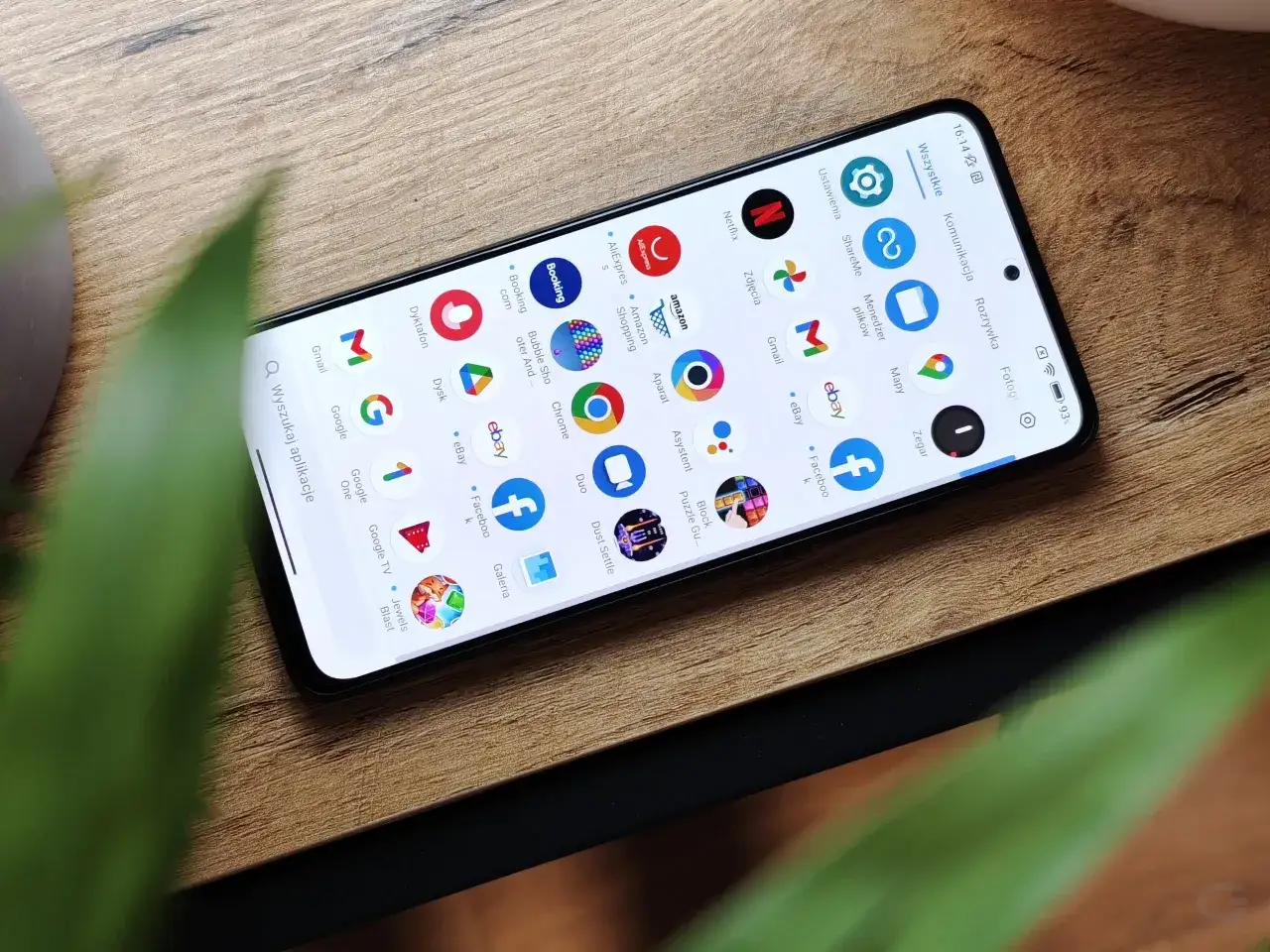 Ekran telefonu Poco X4 z widocznymi ikonami aplikacji, takimi jak Gmail, Netflix, Amazon i eBay, na drewnianym tle.
