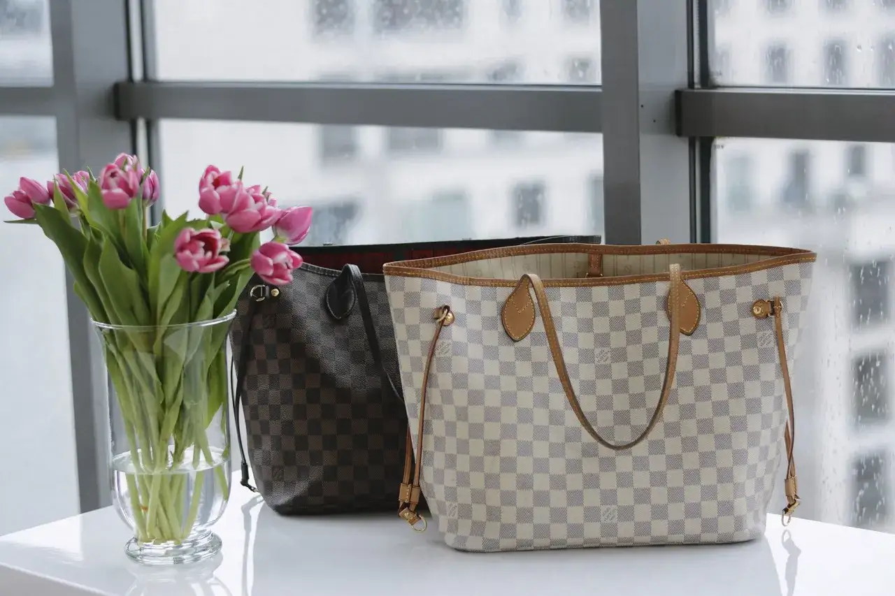 Dwie torebki Louis Vuitton, jedna w jasną kratę, druga w ciemną, obok wazonu z różowymi tulipanami.