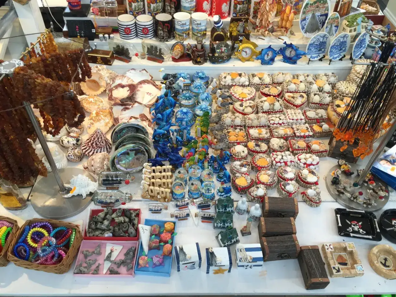 Mnóstwo pamiątek z wakacji: muszle, bursztyny, figurki zwierząt, ozdobne szkatułki i kubki.