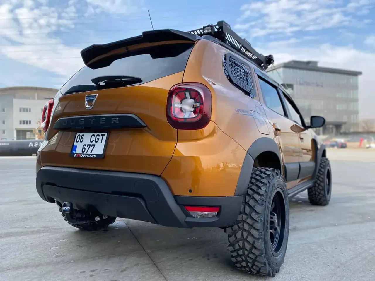 Pomarańczowy Dacia Duster off road z terenowymi oponami i bagażnikiem dachowym, gotowy na przygodę.