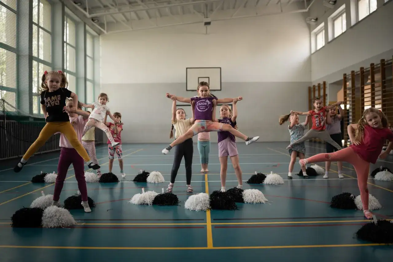Dzieci ćwiczą naukę tańca nowoczesnego w sali gimnastycznej, wykonując akrobatyczne figury.