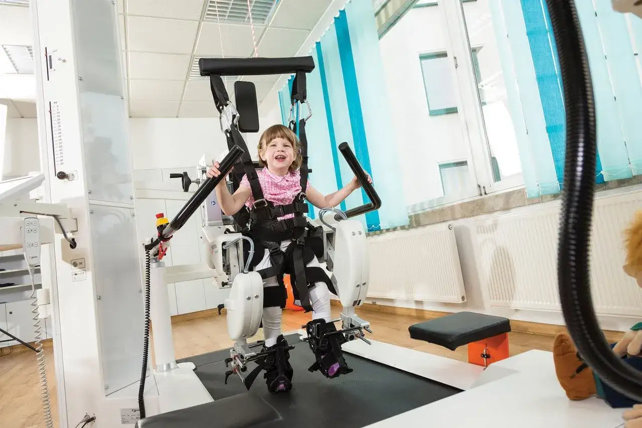Uśmiechnięta dziewczynka w specjalistycznym sprzęcie do rehabilitacji. Czas trwania rehabilitacji dziennej zależy od potrzeb pacjenta.