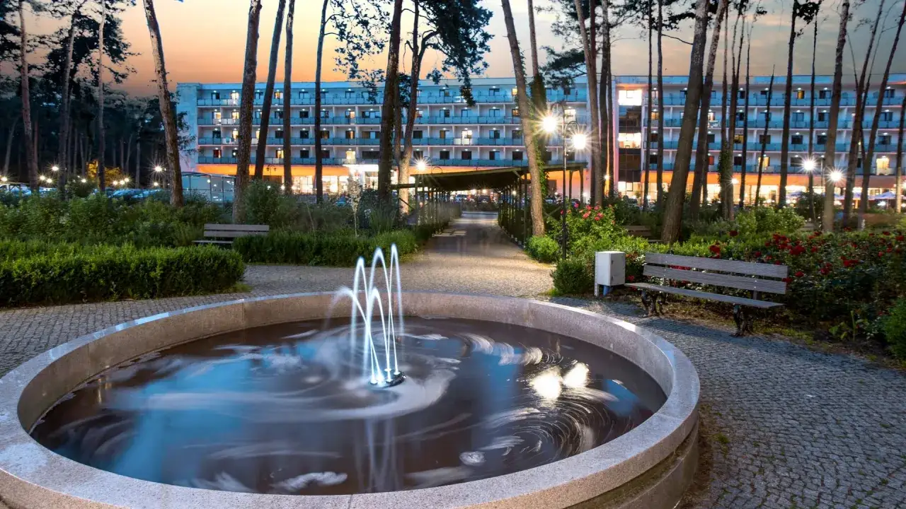Wieniec-Zdr&oacute;j sanatorium: malowniczy park z fontanną i ławkami, oświetlony budynek hotelowy. Sprawdź ceny pobytu!