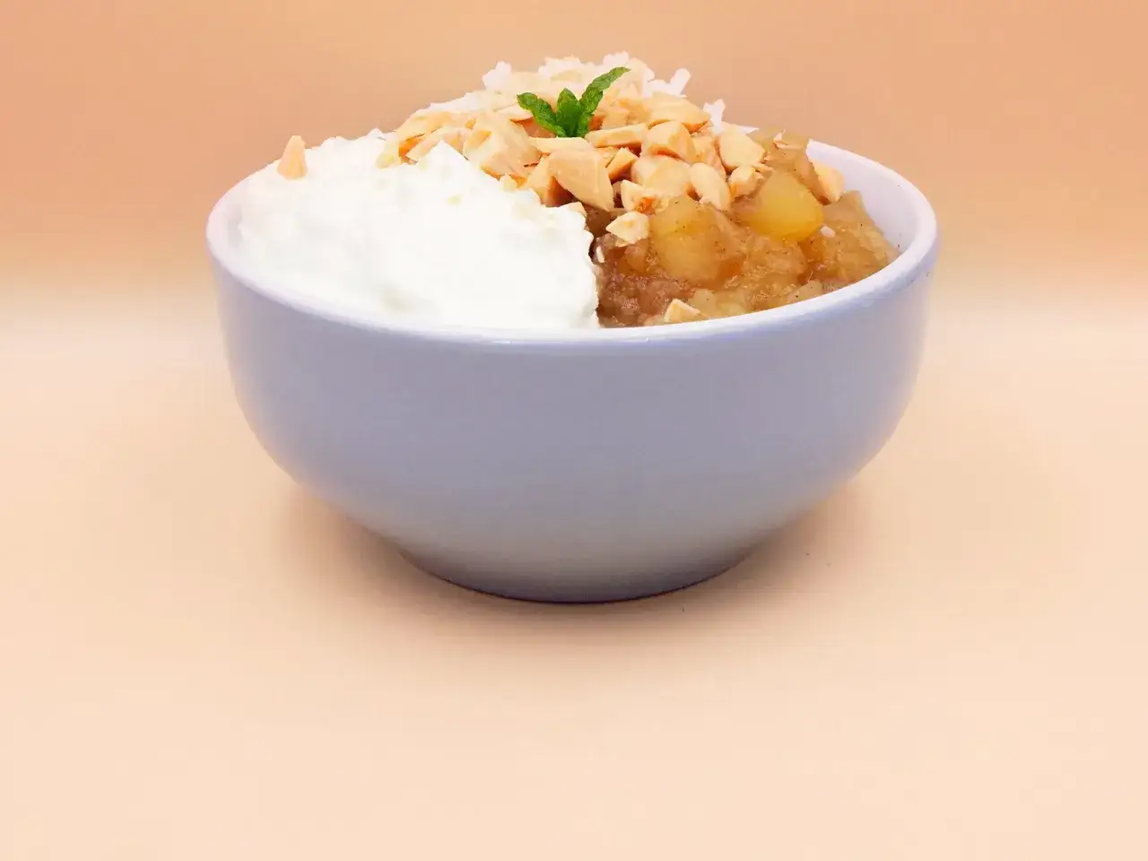 Miseczka z jogurtem i jabłkiem, posypana orzechami i wiórkami kokosowymi. Idealne dla niemowlaka od 6 miesiąca.