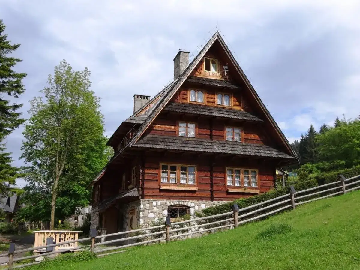 Drewniany dom w górach, idealne miejsce, gdzie szukać noclegów oprócz booking. Otoczony zielenią, z kamienną podmurówką i drewnianym płotem.