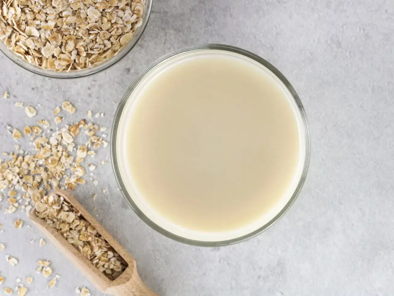 Szklanka mleka owsianego obok płatk&oacute;w owsianych. Czy mleko owsiane ma gluten? Zależy od procesu produkcji.