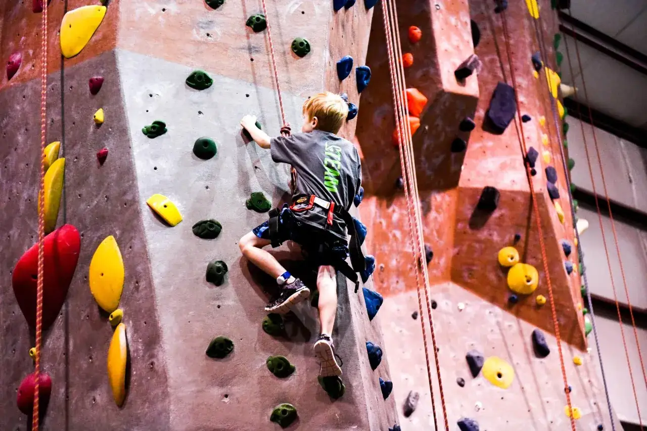 Chłopiec wspina się po kolorowej ścianie wspinaczkowej. To właśnie bouldering – pokonywanie trudnych dróg bez liny, na niewielkiej wysokości.