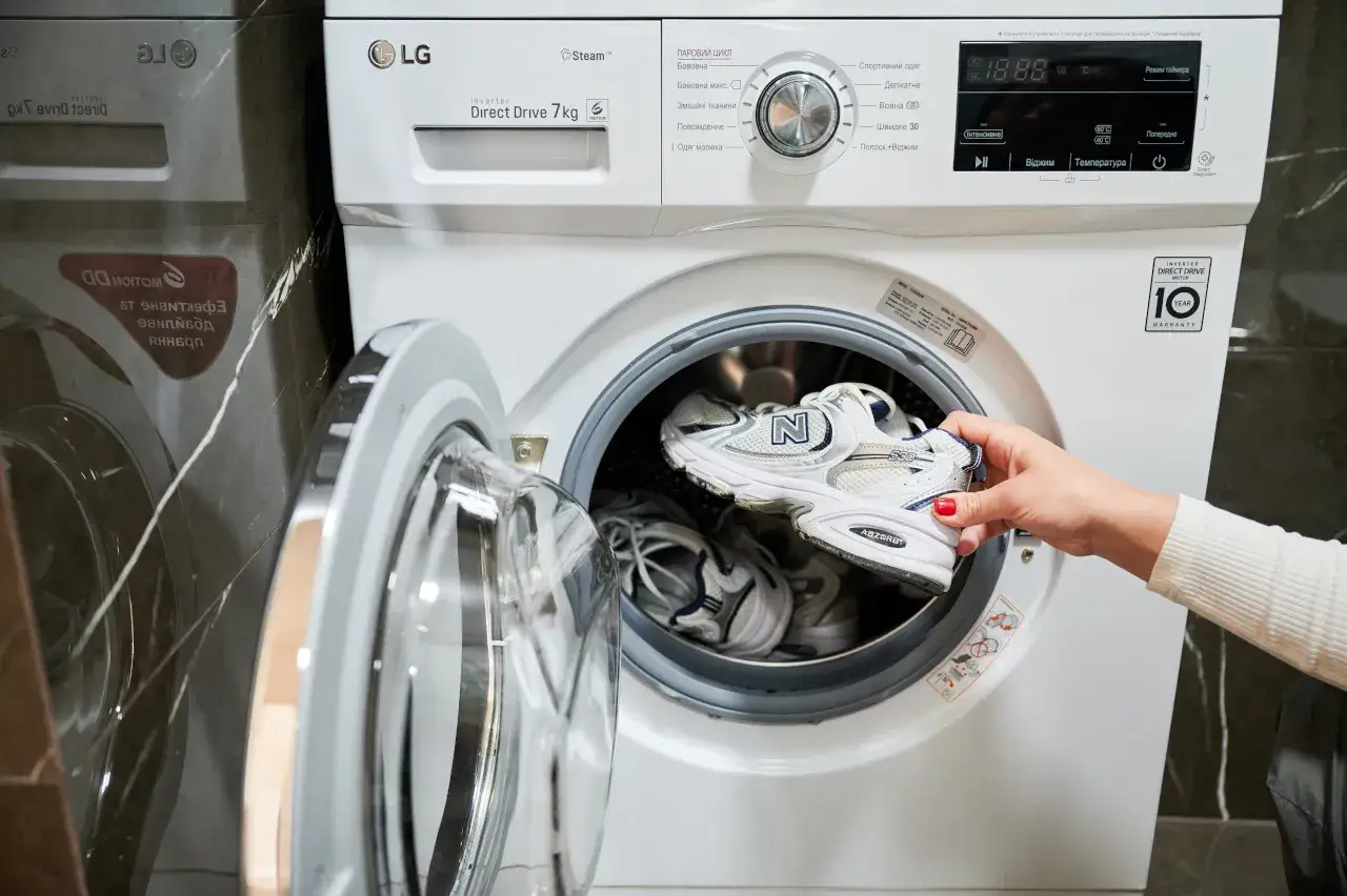 Kobieta wkłada buty do pralki LG. Sprawdź, w ilu stopniach prać buty, aby były czyste i świeże.