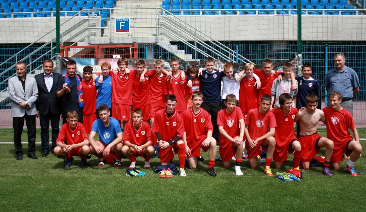 Piast Gliwice zawodnicy w czerwonych strojach pozują do zdjęcia na boisku.