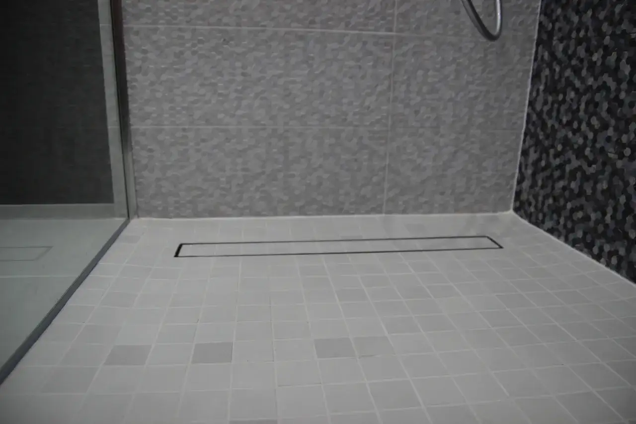 Prysznic z odpływem liniowym. Jasne płytki na podłodze i ścianie, ciemne płytki heksagonalne z boku. Czy fuga jest wodoodporna?