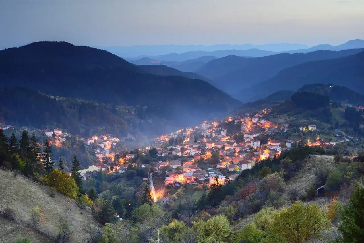 Wieczorna panorama g&oacute;r Pirin z oświetloną wioską w dolinie.
