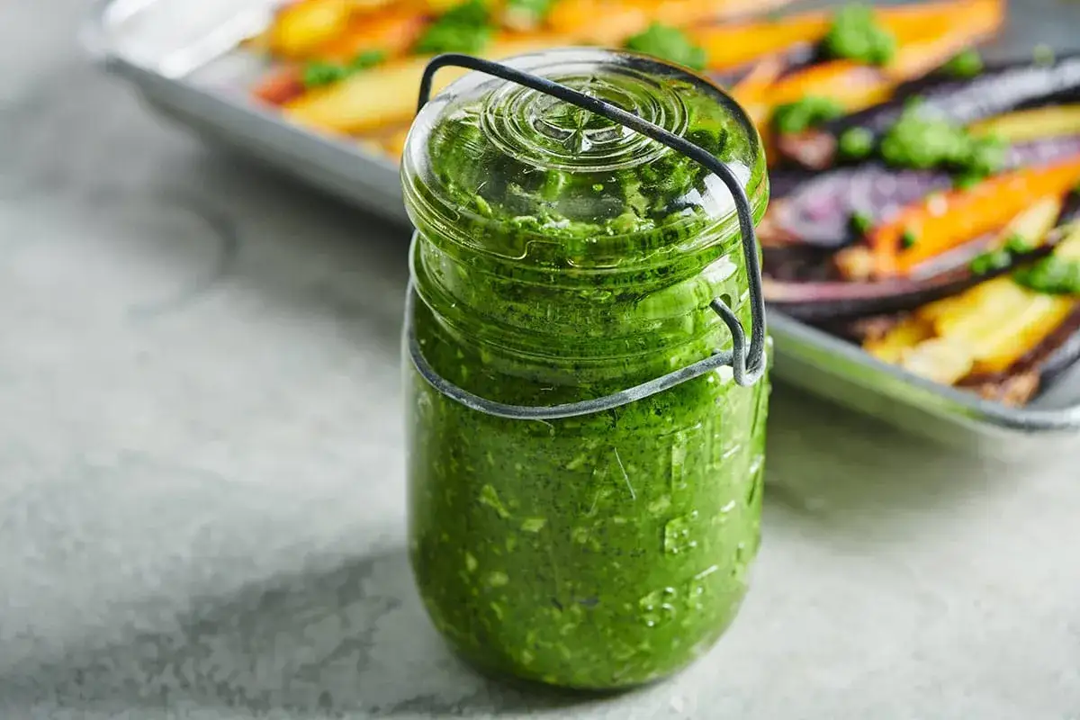 Słoik pełen domowego pesto ze szpinaku, gotowy do słoik&oacute;w. Idealny dodatek do pieczonych warzyw w tle.