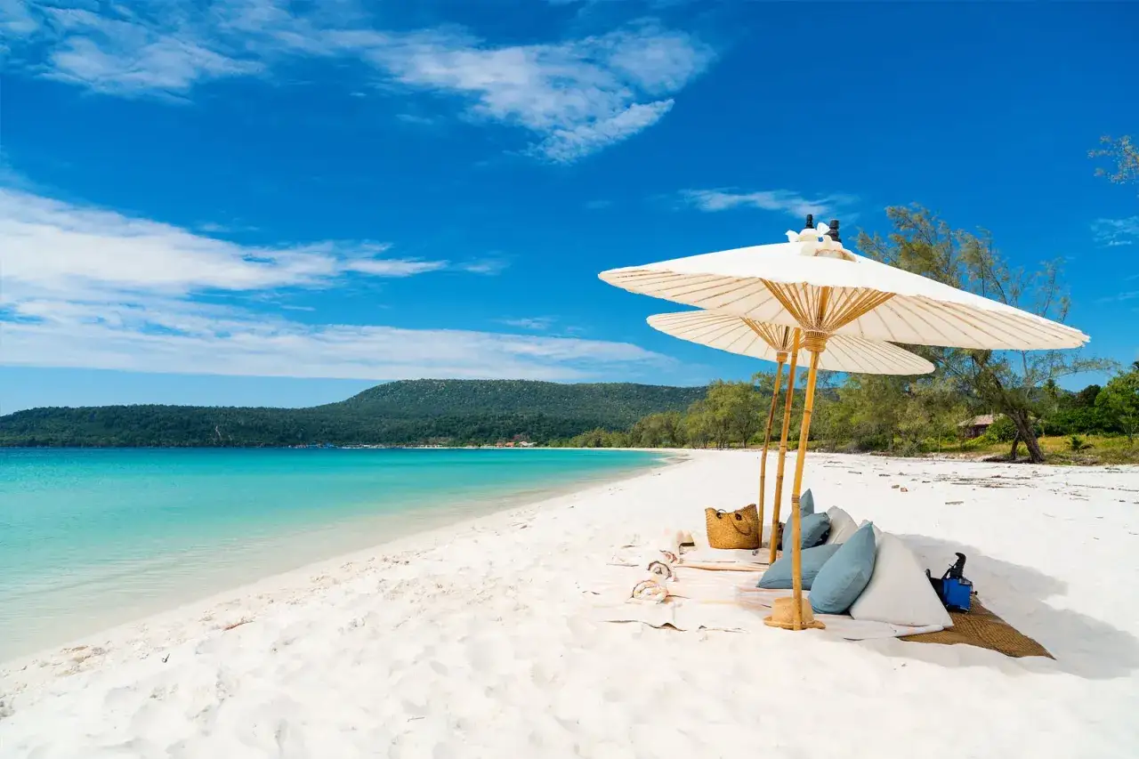 Rajska plaża na Koh Rong, Kambodża. Dwa białe parasole chronią przed słońcem, poduszki i koszyk zapraszają do relaksu.