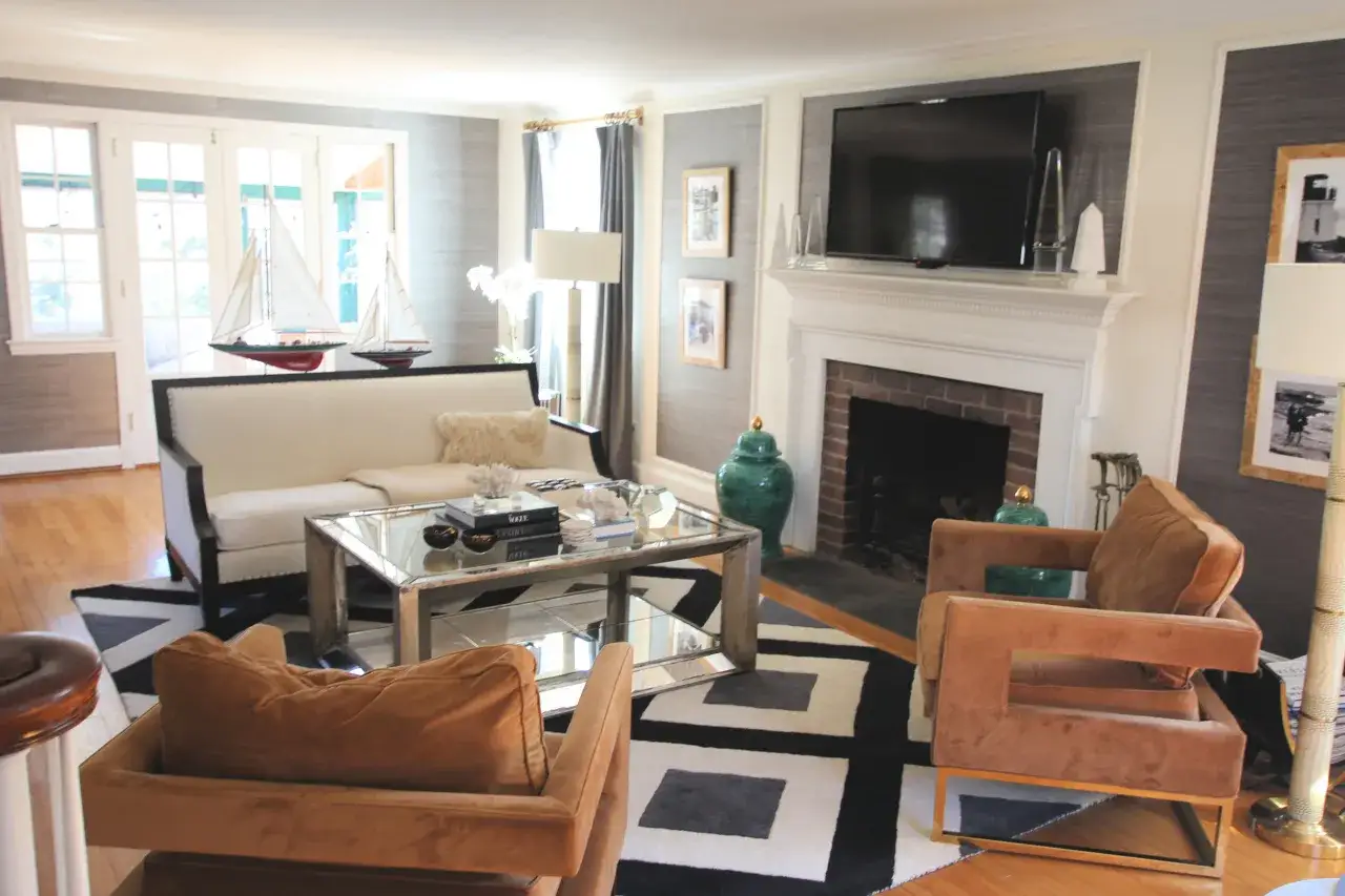 Elegancki salon w stylu kolonialnym z białymi meblami, kominkiem i dekoracjami nawiązującymi do żeglarstwa.