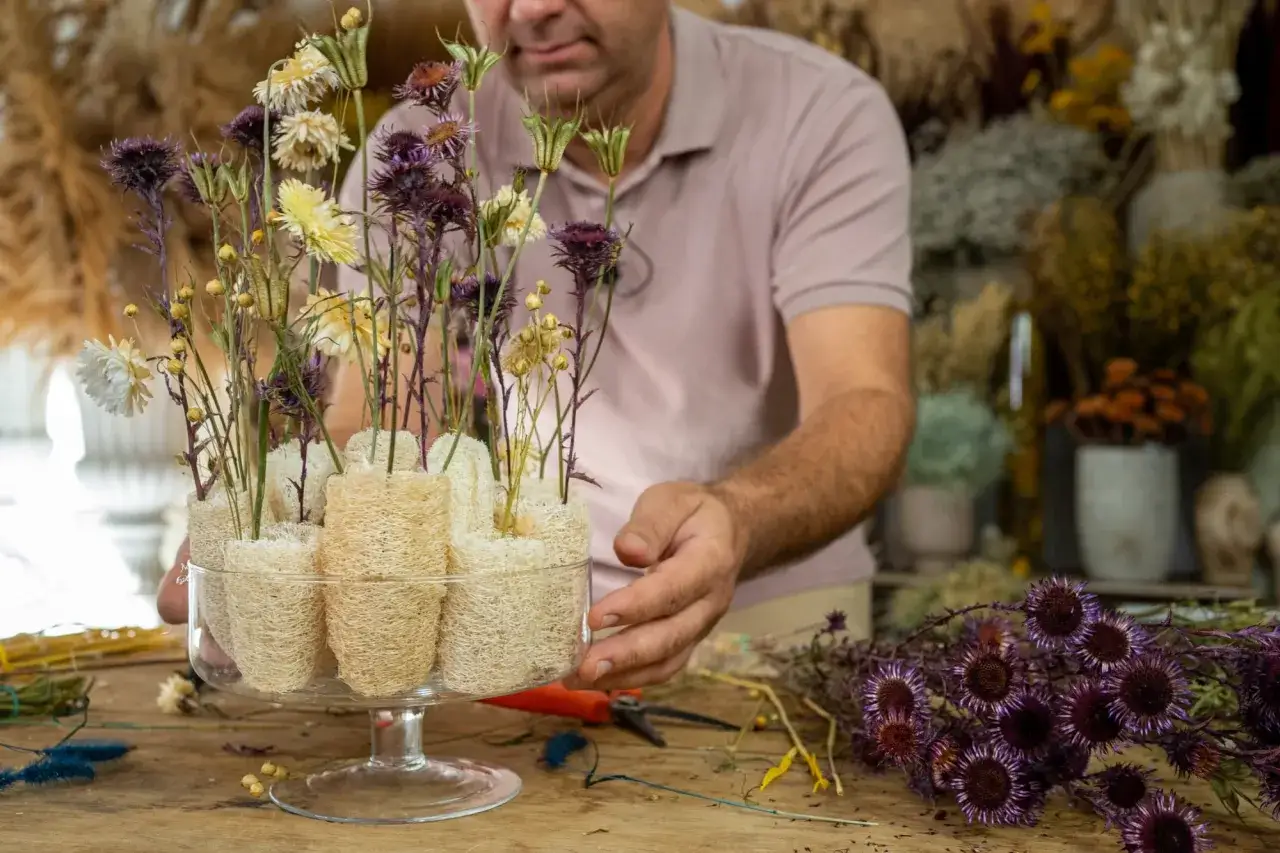 Mężczyzna tworzy kompozycję z suszonych kwiat&oacute;w, pokazując, jak zostać florystą.