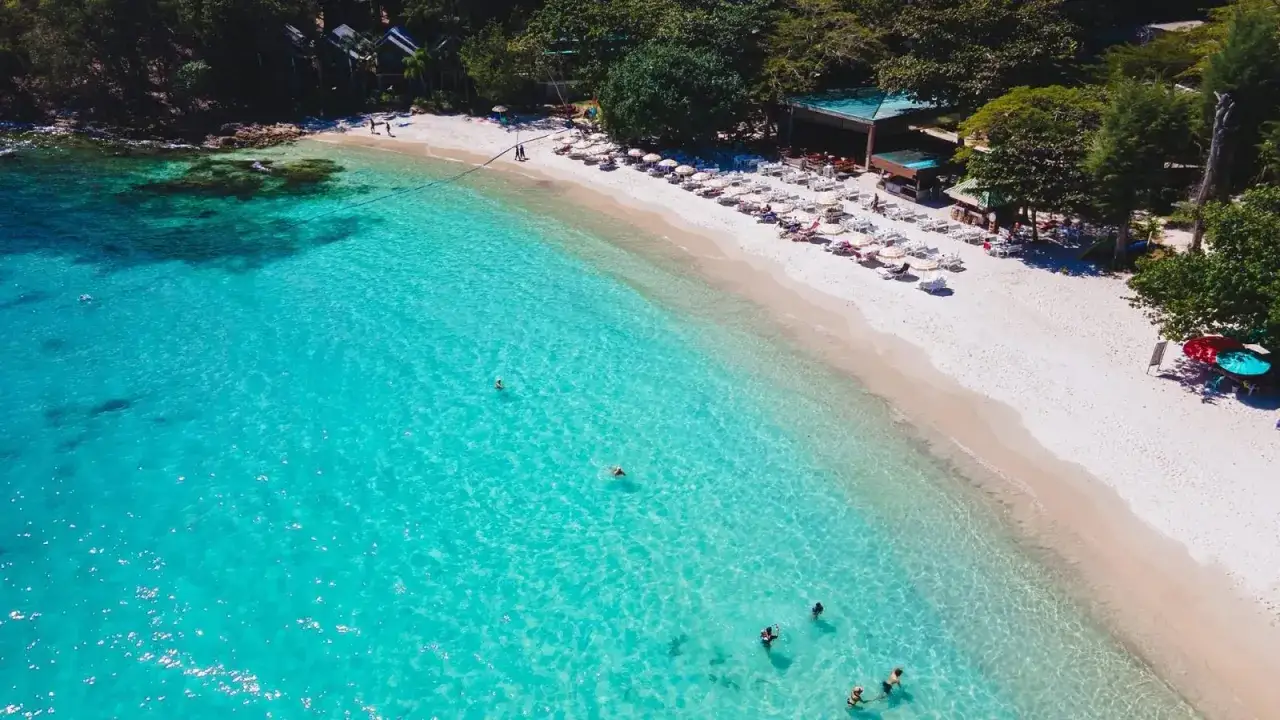 Rajska plaża z turkusową wodą i leżakami. Idealne miejsce na tanie kierunki na wakacje.
