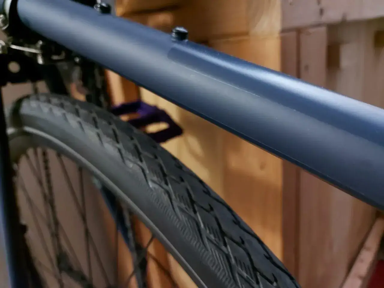 Ciemnoniebieska rama roweru, widoczna opona z bieżnikiem i pedał. Zabezpieczenie ramy roweru przed zarysowaniami.