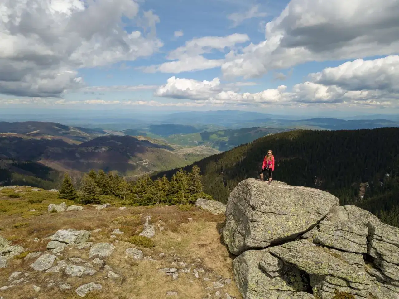 Kobieta na skale podziwia rozległe góry na Półwyspie Bałkańskim. W tle lasy i pagórkowaty krajobraz.