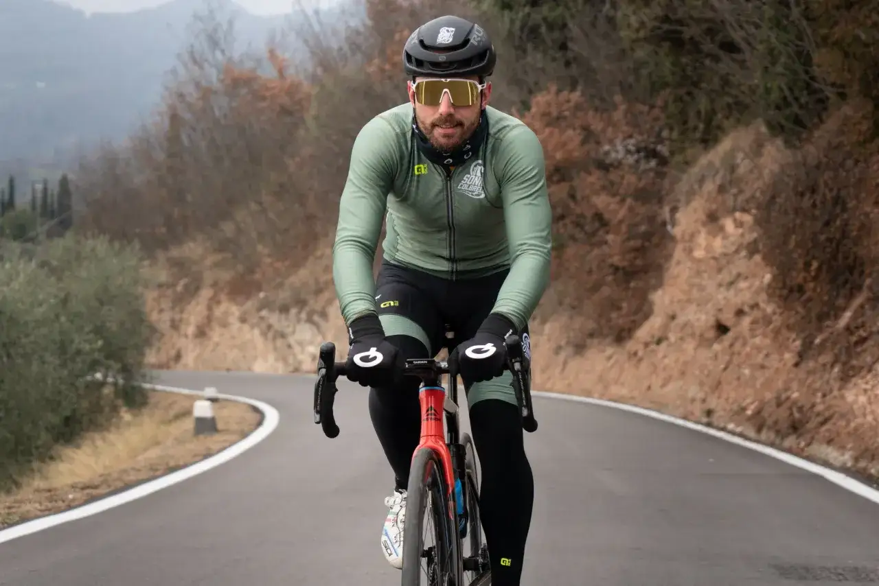 Kolarz w zielonej bluzie i czarnych spodenkach, z ż&oacute;łtymi okularami, zastanawia się, jakie rękawiczki na rower wybrać, by chronić dłonie podczas jazdy po g&oacute;rskiej drodze.