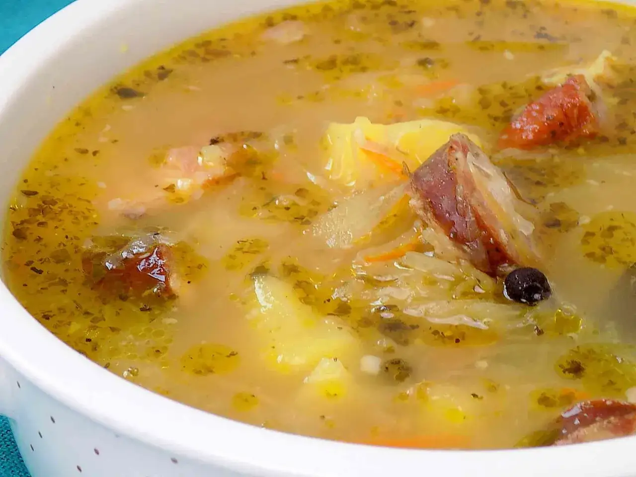 Gęsty kapuśniak z kiszonej kapusty z kawałkami mięsa i ziemniak&oacute;w, doprawiony ziołami i pieprzem.