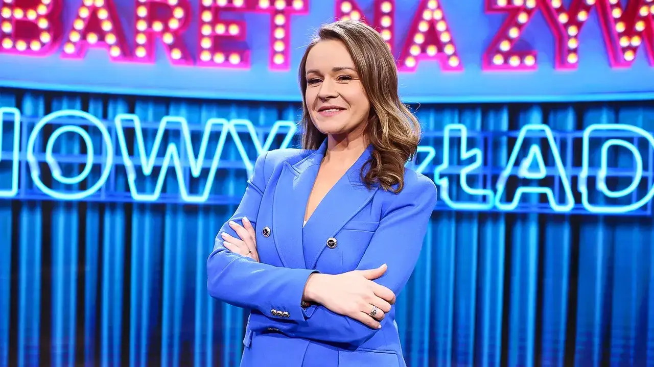 Ewa Błachnio w niebieskiej marynarce na tle neonowego napisu 