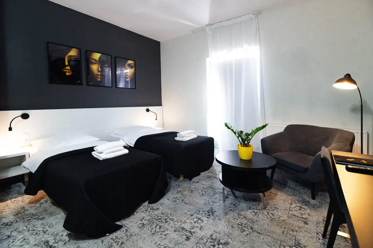 Pokój hotelowy z dwoma łóżkami, czarnymi narzutami i sztuką na ścianie. Dowiedz się, ile trwa doba hotelowa, planując swój pobyt.