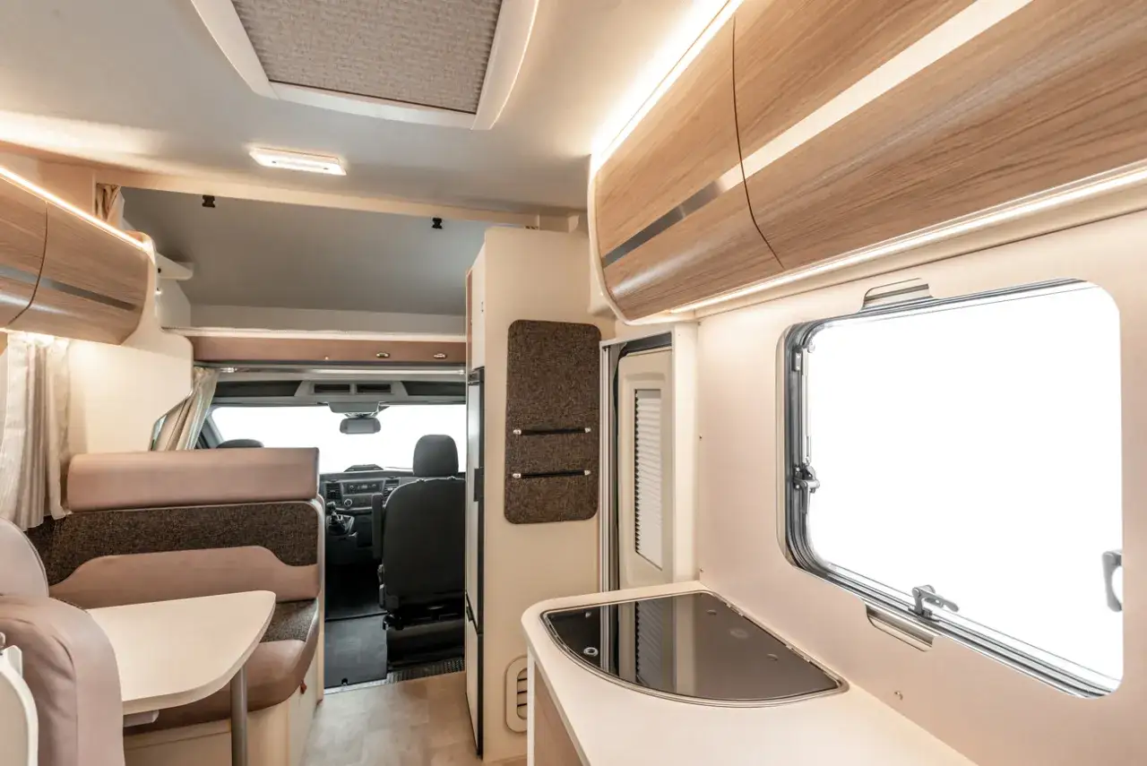 Wnętrze kampera z wygodnym miejscem do siedzenia, aneksem kuchennym i widokiem na kabinę kierowcy. Idealny kamper tanio na podr&oacute;że.