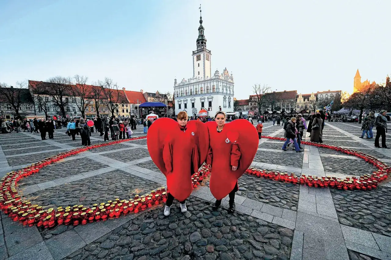Dwie osoby w strojach serc na rynku, otoczone zniczami tworzącymi serce. To miasto zakochanych w Polsce, gdzie miłość rozświetla plac.
