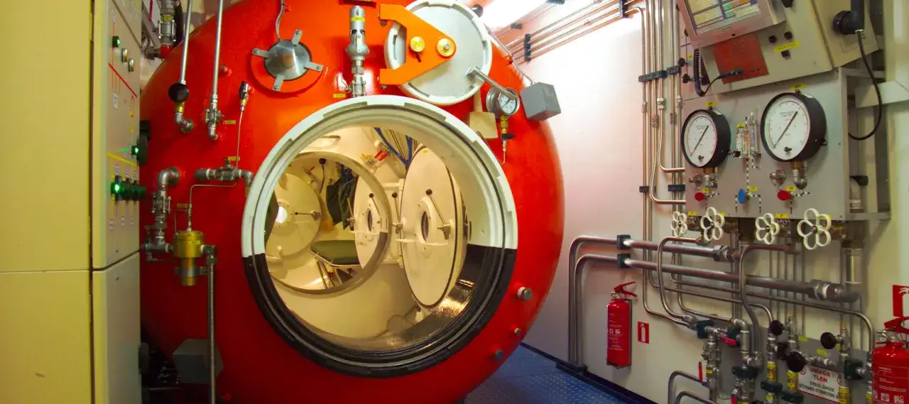 Wnętrze komory dekompresyjnej z widocznymi drzwiami i panelami kontrolnymi. Pokazuje, jak działa komora dekompresyjna, umożliwiając bezpieczne powroty z głębin.